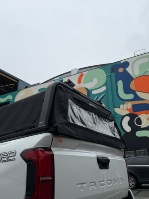 Motu hybrid truck cap with integrated canopy and gear rack on a white Toyota Tacoma in an urban neighborhood.