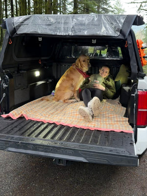 Dog and person under a MOTU hybrid truck cap, integrates a soft top canopy and exoskeleton gear rack on a Toyota Tacoma pickup. Weatherproof. 